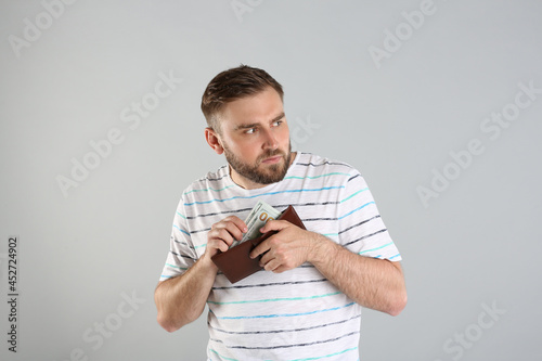 Greedy young man hiding wallet with money on light grey background photo
