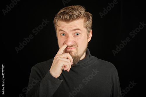 Funny bearded man picking his nose, black background