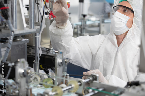 male engineers wearing personal protective equipment uniform(PPE) and medical face mask, checking machine in laboratory