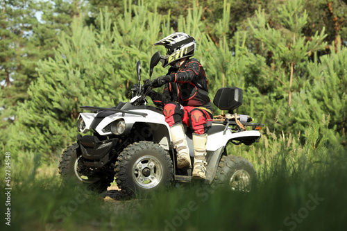 Man driving modern quad bike on sandy road near forest. Extreme sport photo