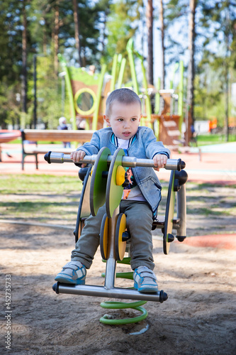 Caucasian little boy riding a swing in the playground outdoors on a sunny day