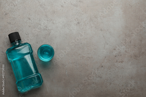Bottle and glass with mouthwash on grey table, flat lay. Space for text
