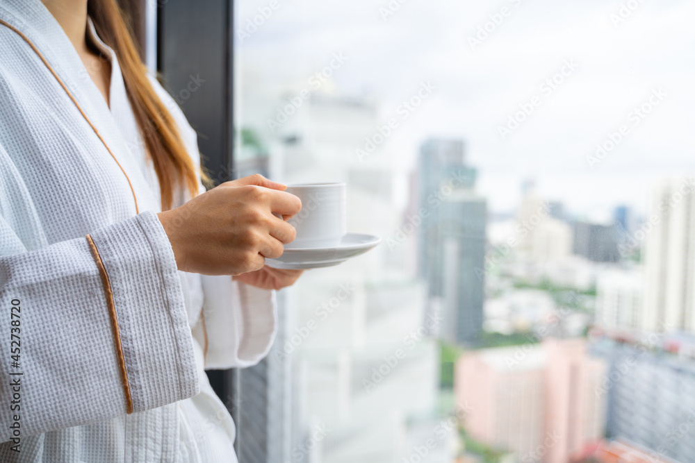 Relaxed Asian woman wearing bath robe drinking coffee in hotel room in morning Relaxed Asian woman wearing bath robe drinking coffee in hotel room in morning