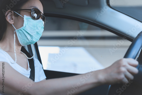 woman driving car with medical mask and sunglasses on her face. Health care and virus protection.