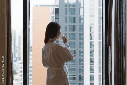 Free Download Relaxed Asian woman wearing bath robe drinking coffee in hotel room in morning  - GFXLoad