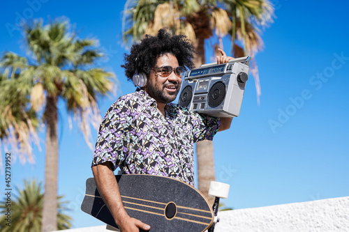 Young african american skater man listening music from vintage boombox stereo on the beach photo