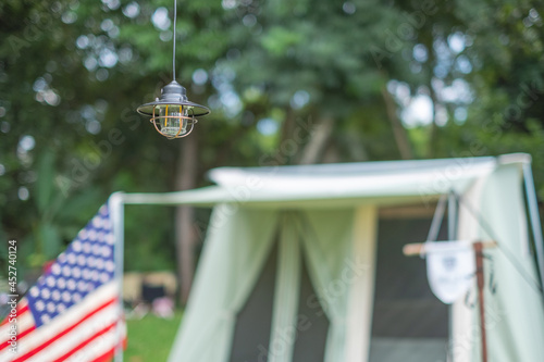 a vintage hanging black camping lantern with blurred background of tents and American flag in the camping area at natural