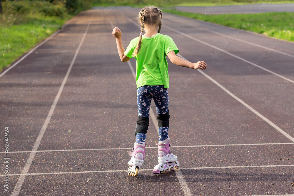 A little girl with pigtails is learning to roller skate on a hard surface. 