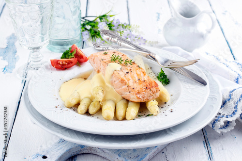 Traditional Altantic fried salmon filet white asparagus in sauce hollandaise and tomatoes served as close-up on a classic design plate