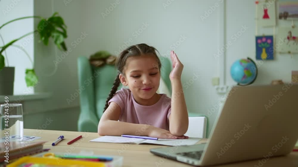 Home education of junior schoolchildren. Spbd Positive little girl raises hand and answers teacher question during online lesson via laptop in room Home education of junior schoolchildren. Spbd Positive little girl raises hand and answers teacher question during online lesson via laptop in room