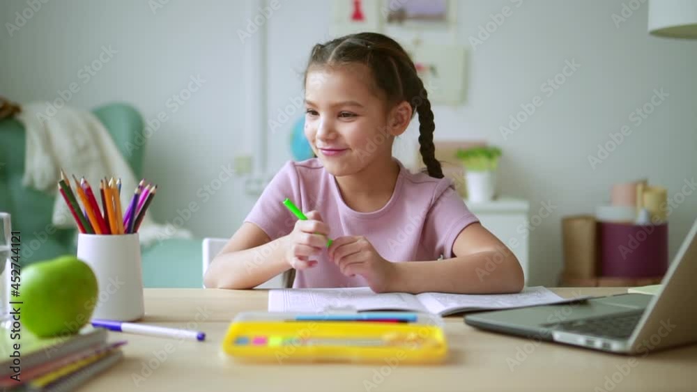 Online primary school education. Spbd Pretty brunette schoolgirl changes marker doing classwork during video lesson via modern laptop at desk in light room Online primary school education. Spbd Pretty brunette schoolgirl changes marker doing classwork during video lesson via modern laptop at desk in light room
