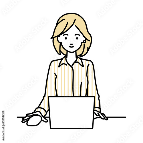 デスクで座ってPCを使っているブラウスの女性