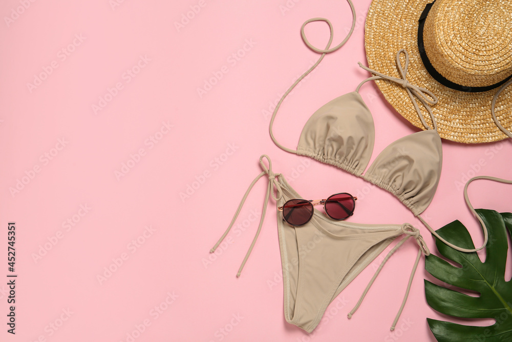 Obraz premium Stylish bikini, straw hat, sunglasses and tropical leaf on pink background, flat lay. Space for text