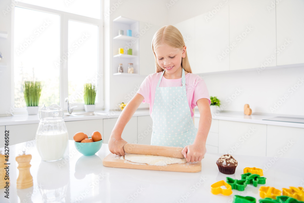 Photo of cheerful happy little girl hold rolling pin make dough cake hobby indoors inside house kitchen Photo of cheerful happy little girl hold rolling pin make dough cake hobby indoors inside house kitchen