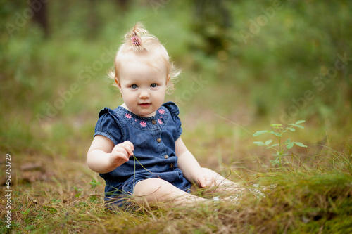 a little girl in a blue dress is sitting on the grass in the park in summer