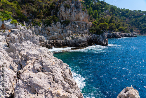 Stony coast from rocks and green trees and bushes by the sea, concept of vacation 