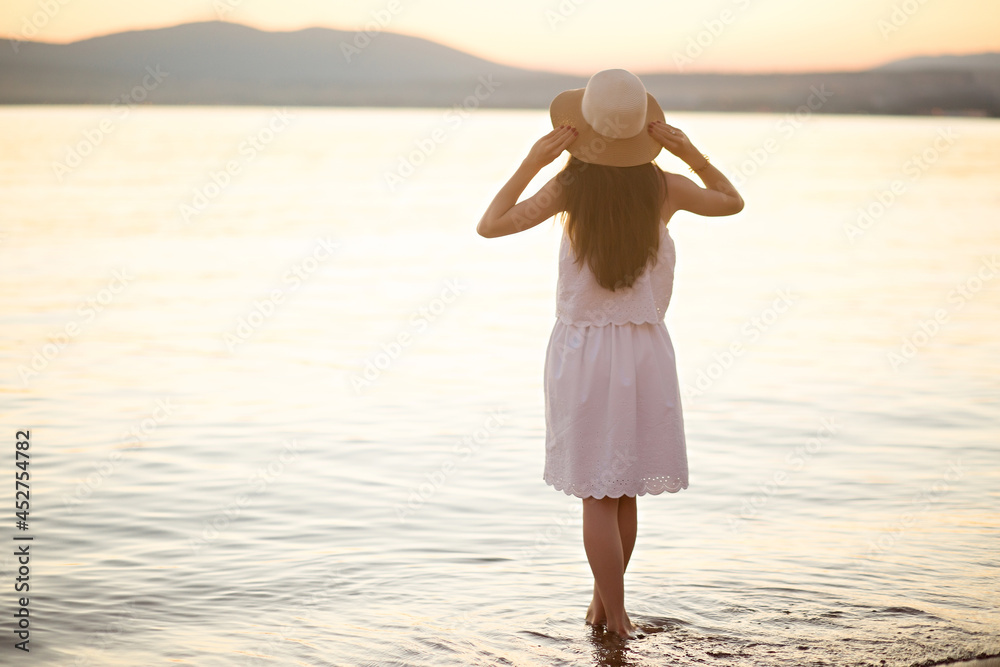 a girl in a hat on the beach in a white dress