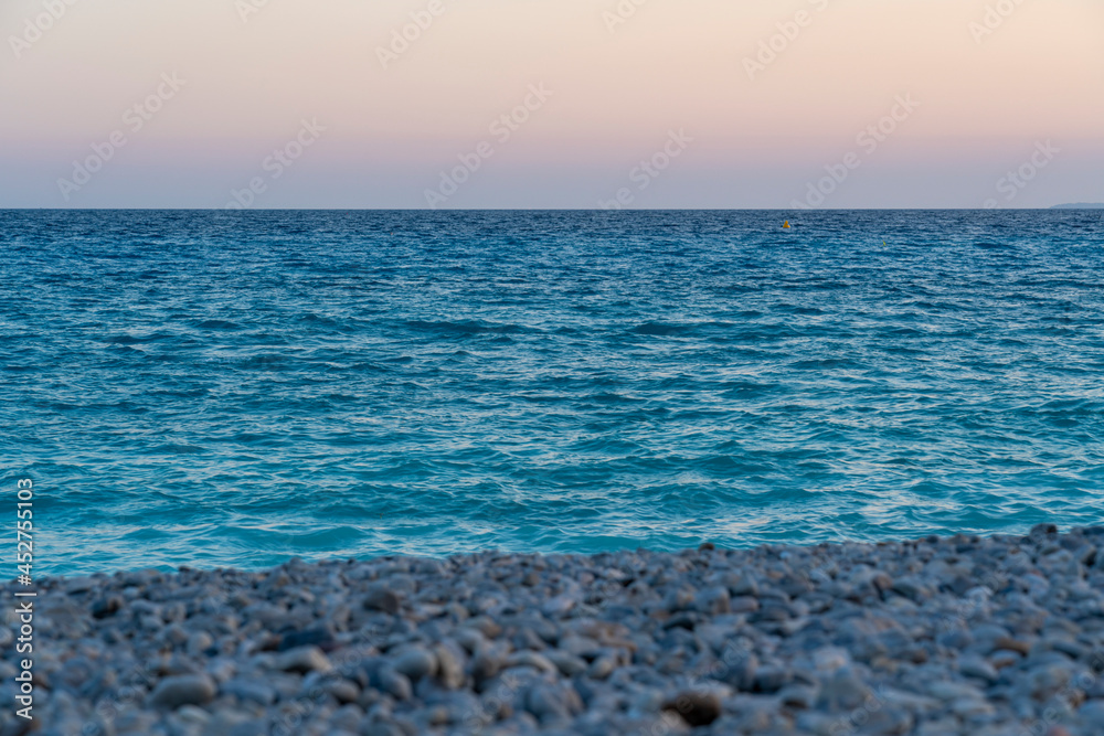 Stony pebble beach in sunset mood and blue sea water, concept of vacation, wanderlust and freedom 