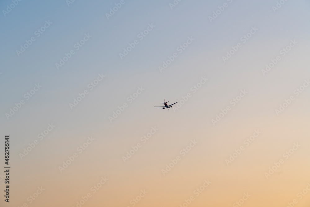 Airplane is flying in the cloudless sky colored by the sunset, concept of vacation and freedom 