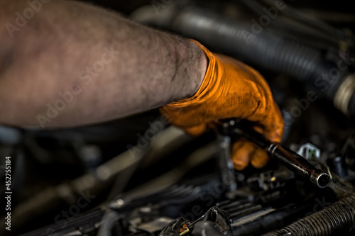 A man wearing an orange glove fixing and doing maintenace on a car engine in an auto repair shop