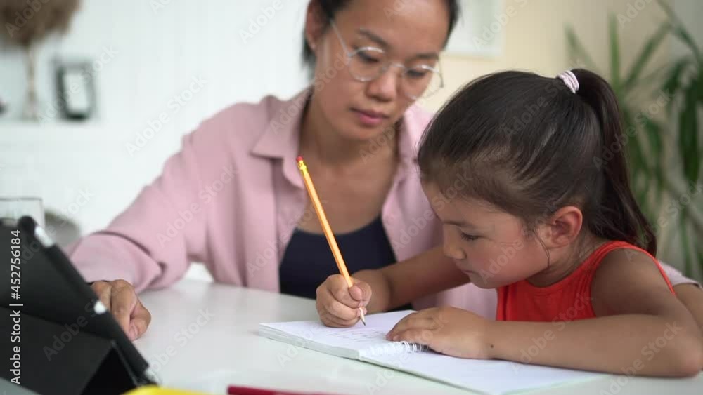 Home people lockdown: young woman helping girl in education and sitting at table with tablet spbd. Korean mom helps daughter do homework and talks with smile, child writes in notebook and sits at desk Home people lockdown: young woman helping girl in education and sitting at table with tablet spbd. Korean mom helps daughter do homework and talks with smile, child writes in notebook and sits at desk