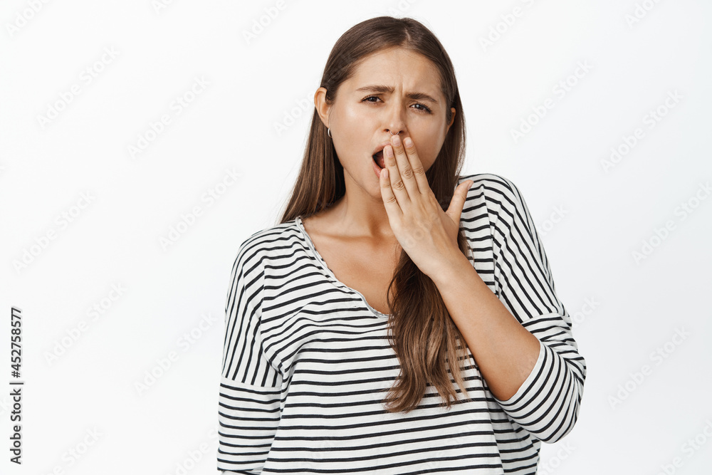 Young woman yawning, looking bored and unamused at camera, white background Young woman yawning, looking bored and unamused at camera, white background