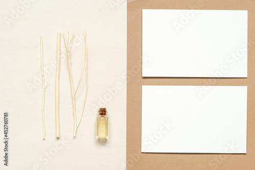 Top view of essential oils in a small transparent glass bottles and diffuser reeds sticks placed on blank white mock up card placed on beige and brown background, copy space.