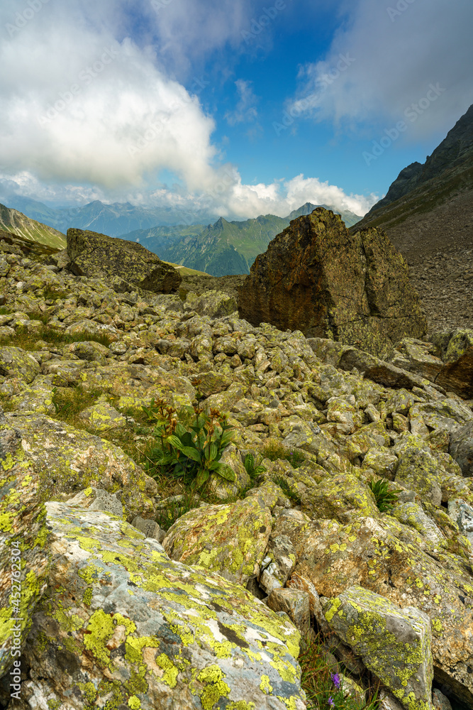 grosse Felsen liegen auf den steinigen Abhängen der Berge im Rhätikon. Wolken ziehen an den Berghängen vorbei und erzeugen eine mystische Stimmung