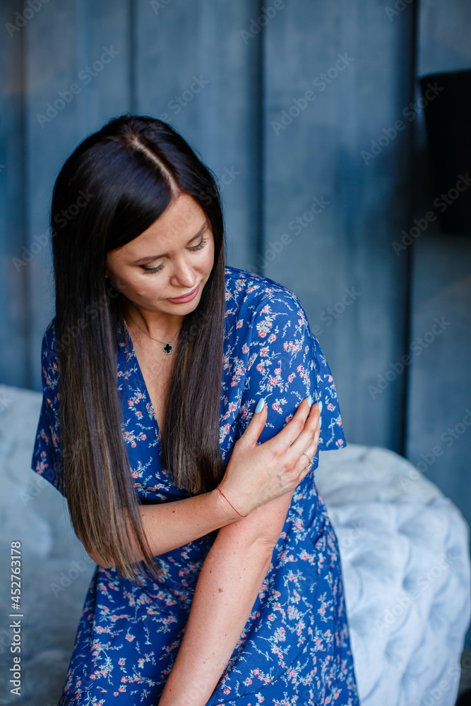 Fototapeta premium Beautiful brunette girl in a blue dress in a room with a gray sofa