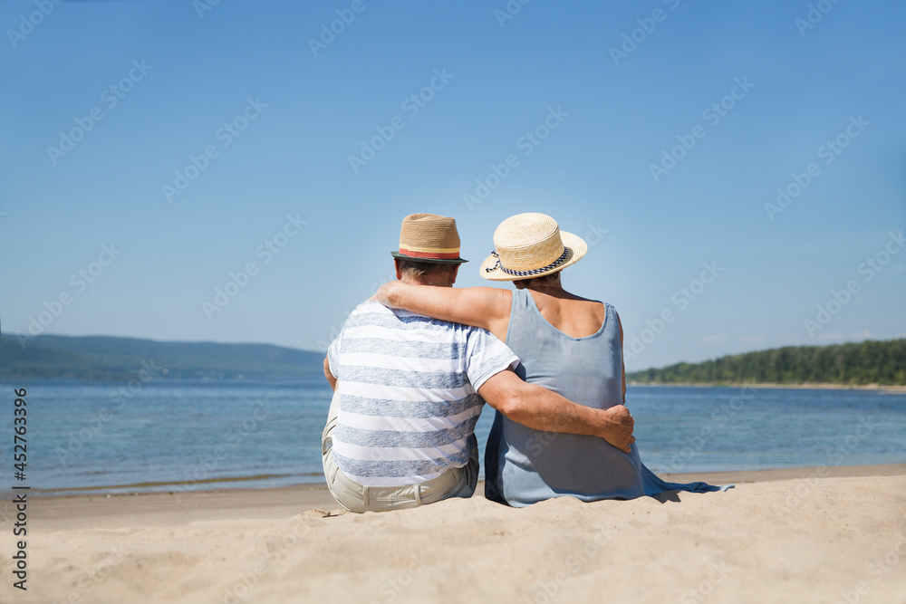 Portrait of senior couple embracing and sitting on the beach sea on a sunny day together