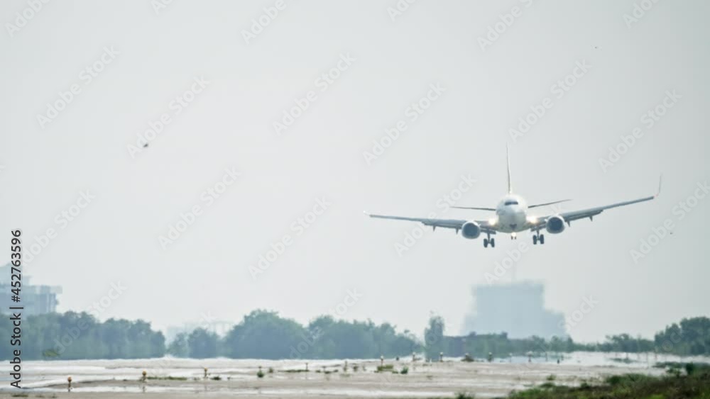 Slow motion video of a plane landing at the airport. The plane flies it sways in the wind and the wheels touch the runway in urban landscapes.