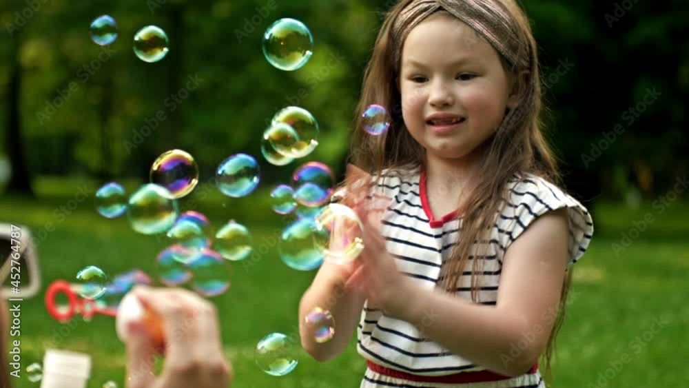 A 6-year-old girl happily catches rainbow bubbles that her mother blows. Family holiday. A 6-year-old girl happily catches rainbow bubbles that her mother blows. Family holiday.