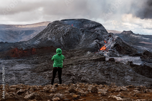 Anonymous tourist admiring erupting volcano under cloudy sky