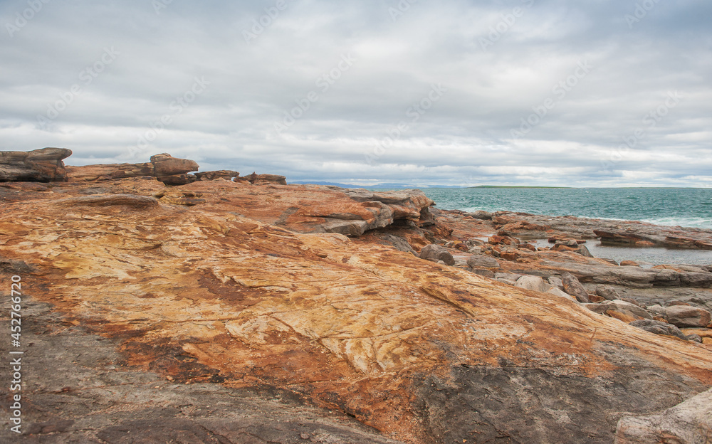 Big boulders of red rock and sea waves against the dramatic sky background