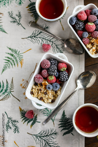 Oatmeal in square ceramic bowls with frozen berries. Porridge with raspberries, blackberries, blueberries and strawberries in white plates on a wooden table with a tablecloth.
