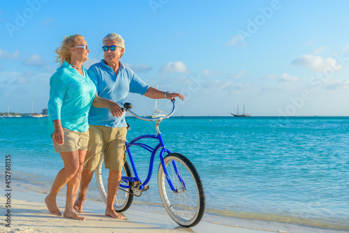Older couple, seniors, riding bicycles on the beach in tropical blue outfits at sunset, romantic, fitness