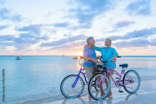 Older couple, seniors, riding bicycles on the beach in tropical blue outfits at sunset, romantic, fitness