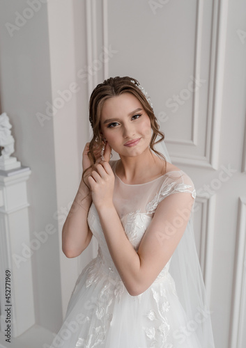 A beautiful young girl in a wedding dress and a veil on a white background with hair and makeup, a smile, happiness.