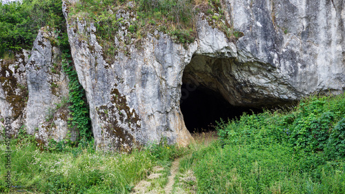 The entrance to the cave in the rock with grass in the foreground.