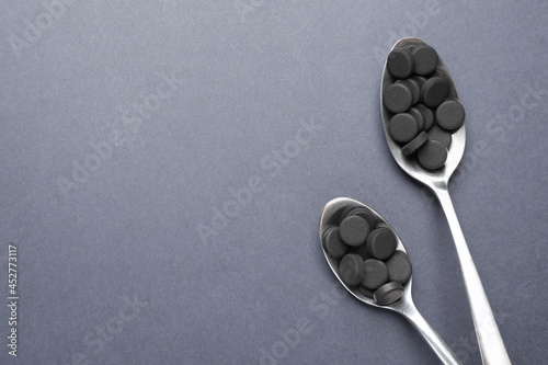 Activated charcoal pills in spoons on grey background, flat lay with space for text. Potent sorbent photo