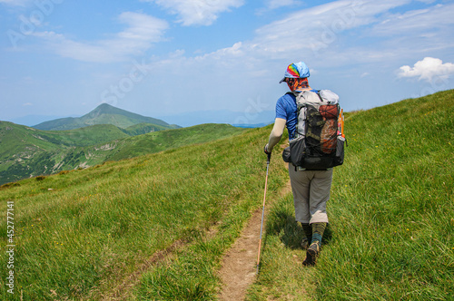A sports tourist with a large backpack walks along a mountain trail in the Ukrainian carpathians overlooking Hoverla, the highest mountain in Ukraine