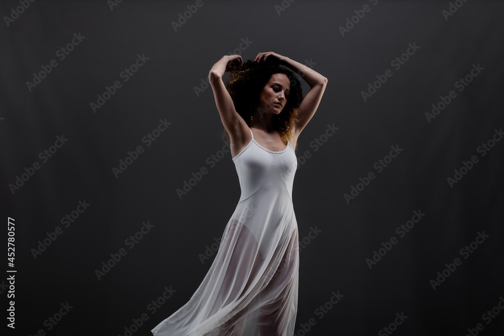 Girl with curly hair making ballet poses. Side lit silhouette of ballerina in white dress and black boots against black background. Girl with curly hair making ballet poses. Side lit silhouette of ballerina in white dress and black boots against black background.