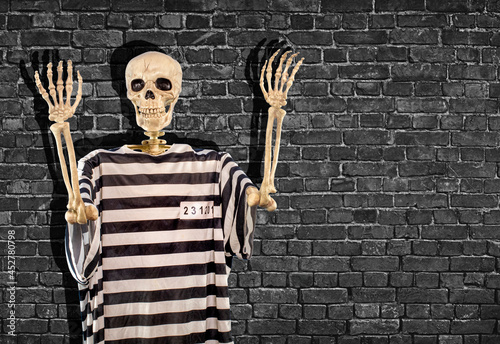 Obraz na plátně Skeleton wearing a inmate halloween costume with hands up and a dark black brick