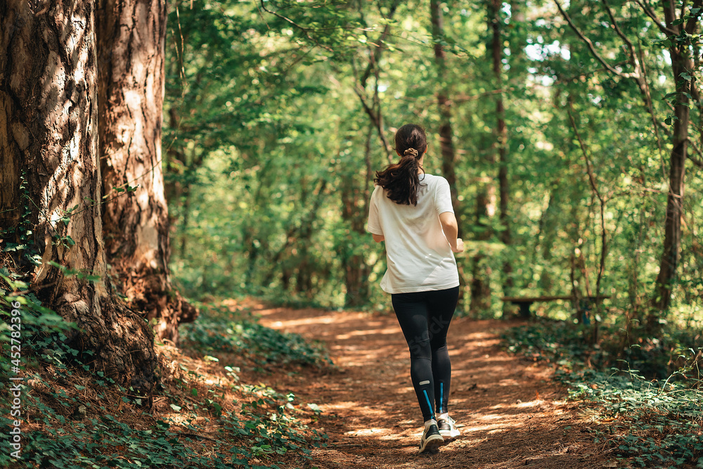 Cross-country running. A young woman in sports clothes is jogging in the morning summer forest. Back view. Concept of outdoor training Cross-country running. A young woman in sports clothes is jogging in the morning summer forest. Back view. Concept of outdoor training