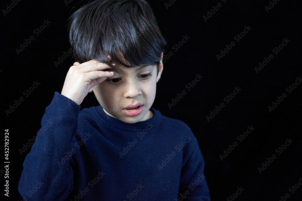 closeup portrait of latin boy looking down pensive and worry with one hand on his head. black background and copy space closeup portrait of latin boy looking down pensive and worry with one hand on his head. black background and copy space