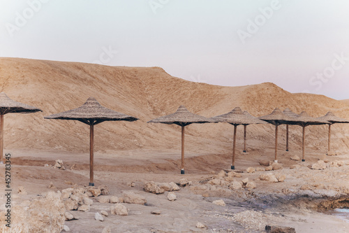 Sandy and rocky coast with palm beach umbrellas in paspel colors. Desolate resort beidge beach on the coast shore of Red Sea. Sharm el Sheikh, Sinai, Egypt, Asia. Travel in the time of coronavirus. photo