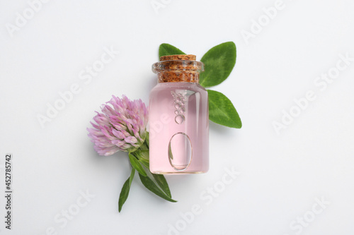 Beautiful clover flower and bottle of essential oil on white background, flat lay