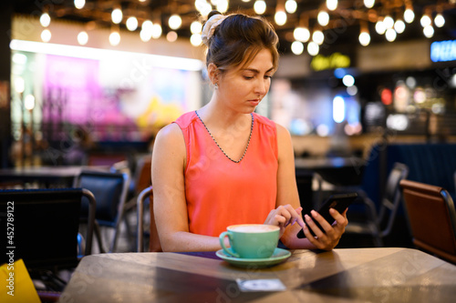 Young woman using her smartphone to browse web content and sending messages while taking a coffee in a bar