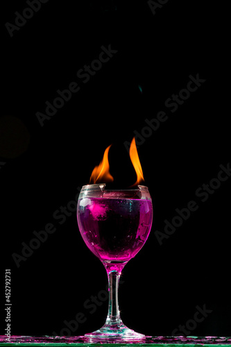 Taça de cristal com bebida cor de rosa, gelada e labaredas de fogo. photo