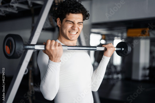 An athlete trains in the gym. Exercise with a barbell, a healthy lifestyle. A man does exercises for biceps endurance and cardio.